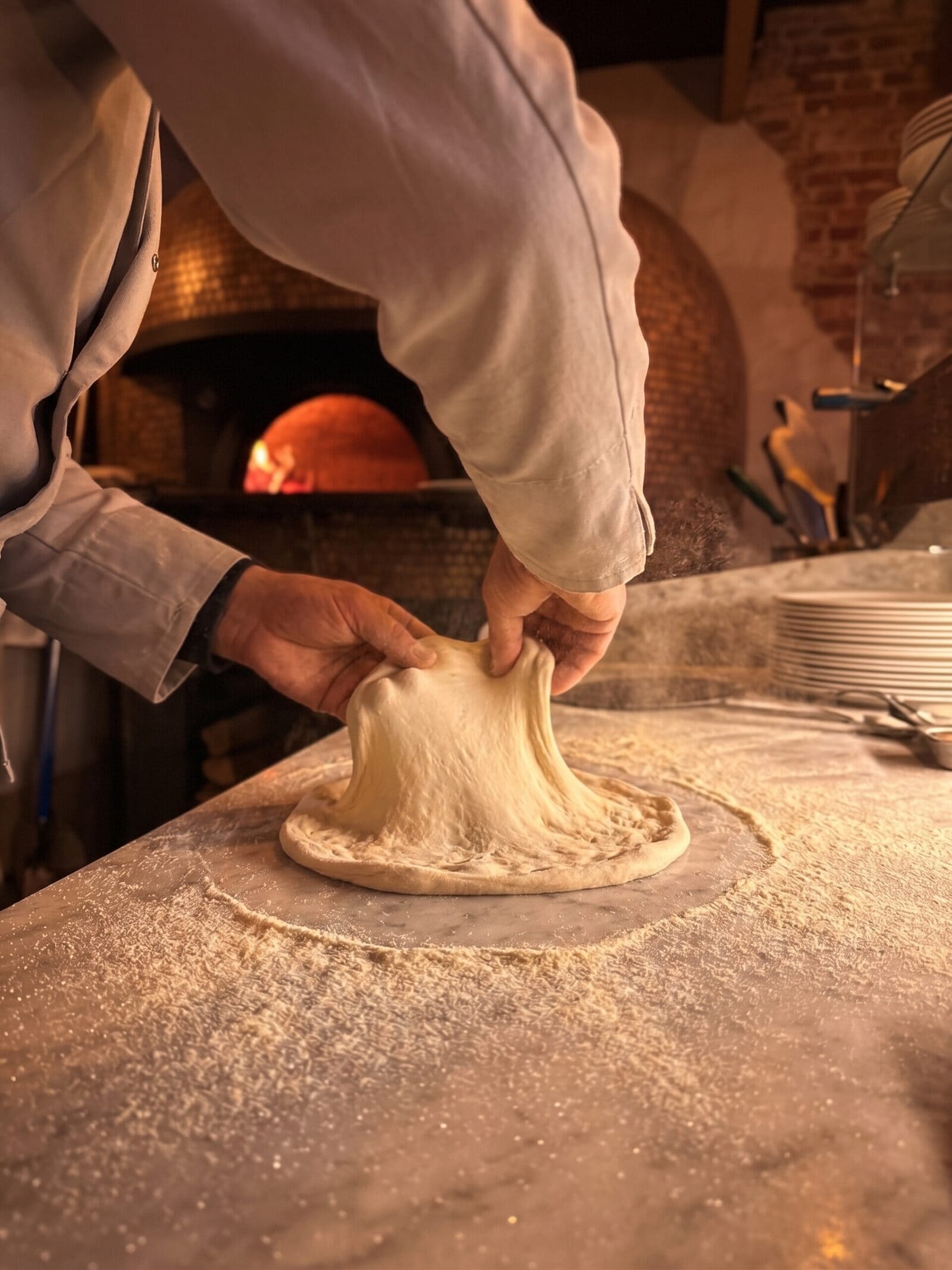 Les mains du pizzaiolo étirant la pâte devant le four à bois